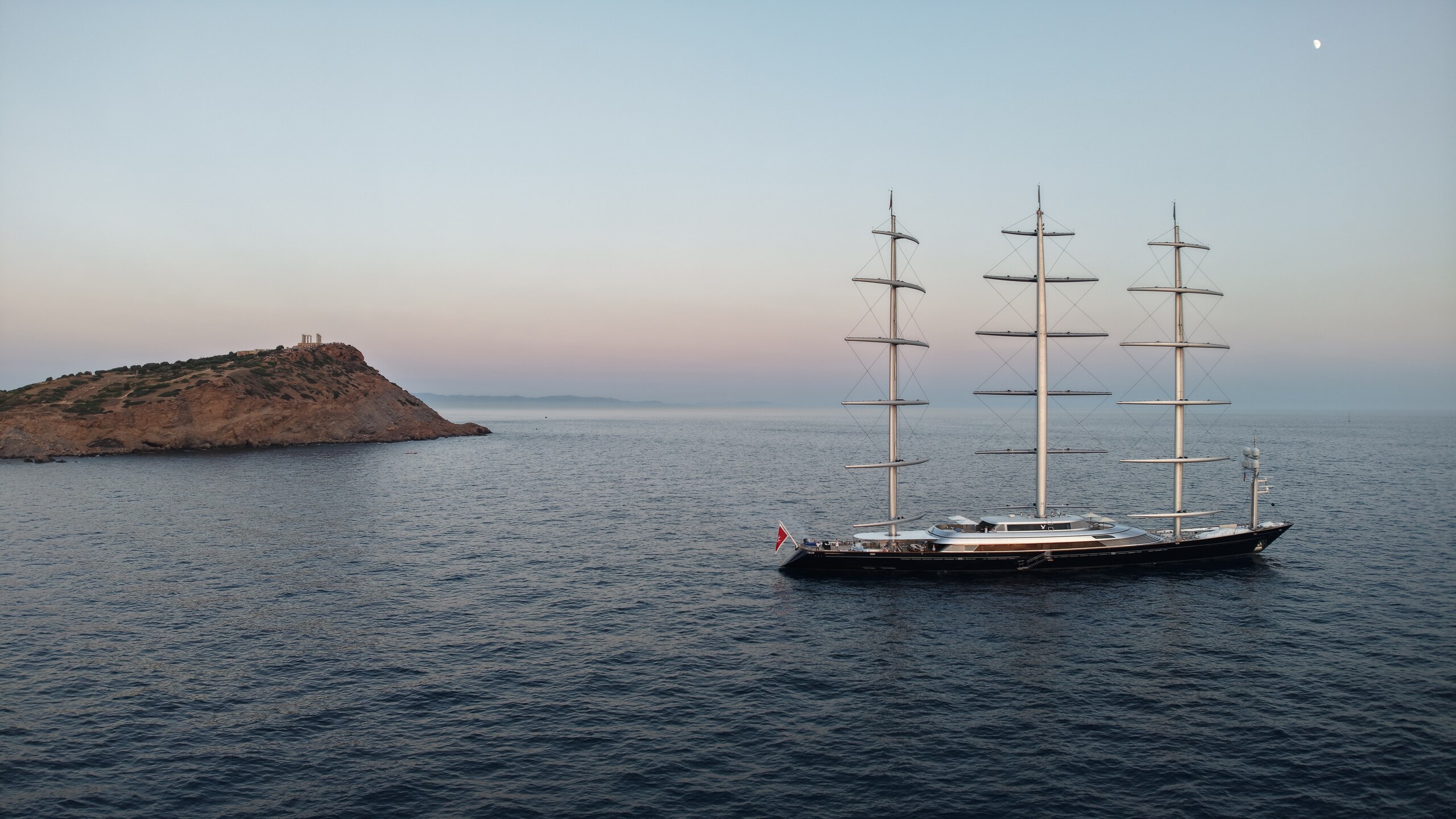 Three-masted sailing yacht near a Greek island at dusk